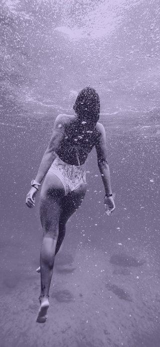 A swimmer underwater in a cloud of bubbles, seen from behind.